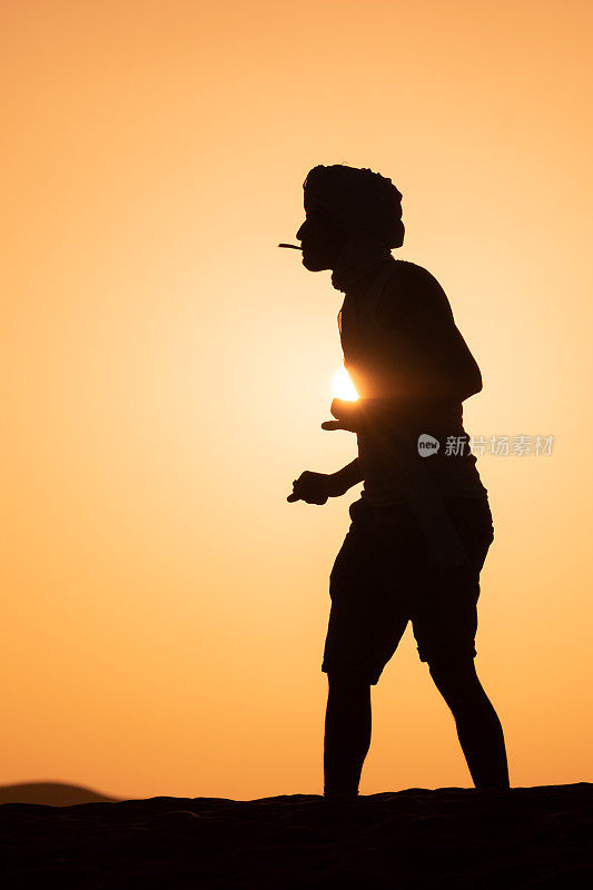 Young man walks across sand dune at sunrise